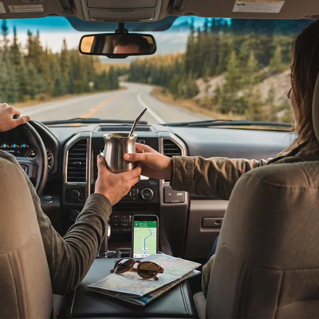 A copilot passing a yerba mate gourd to the driver during a summer road trip through the mountains.