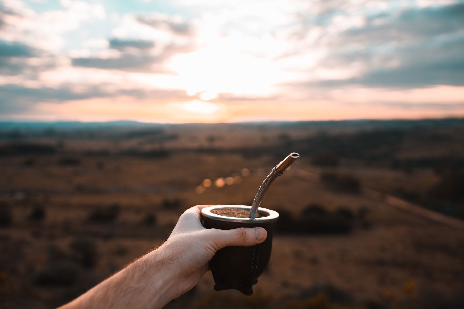 Close-up of a hand holding an authentic mate gourd and bombilla at sunset, showcasing the traditional ritual by Luv Mate in Alberta