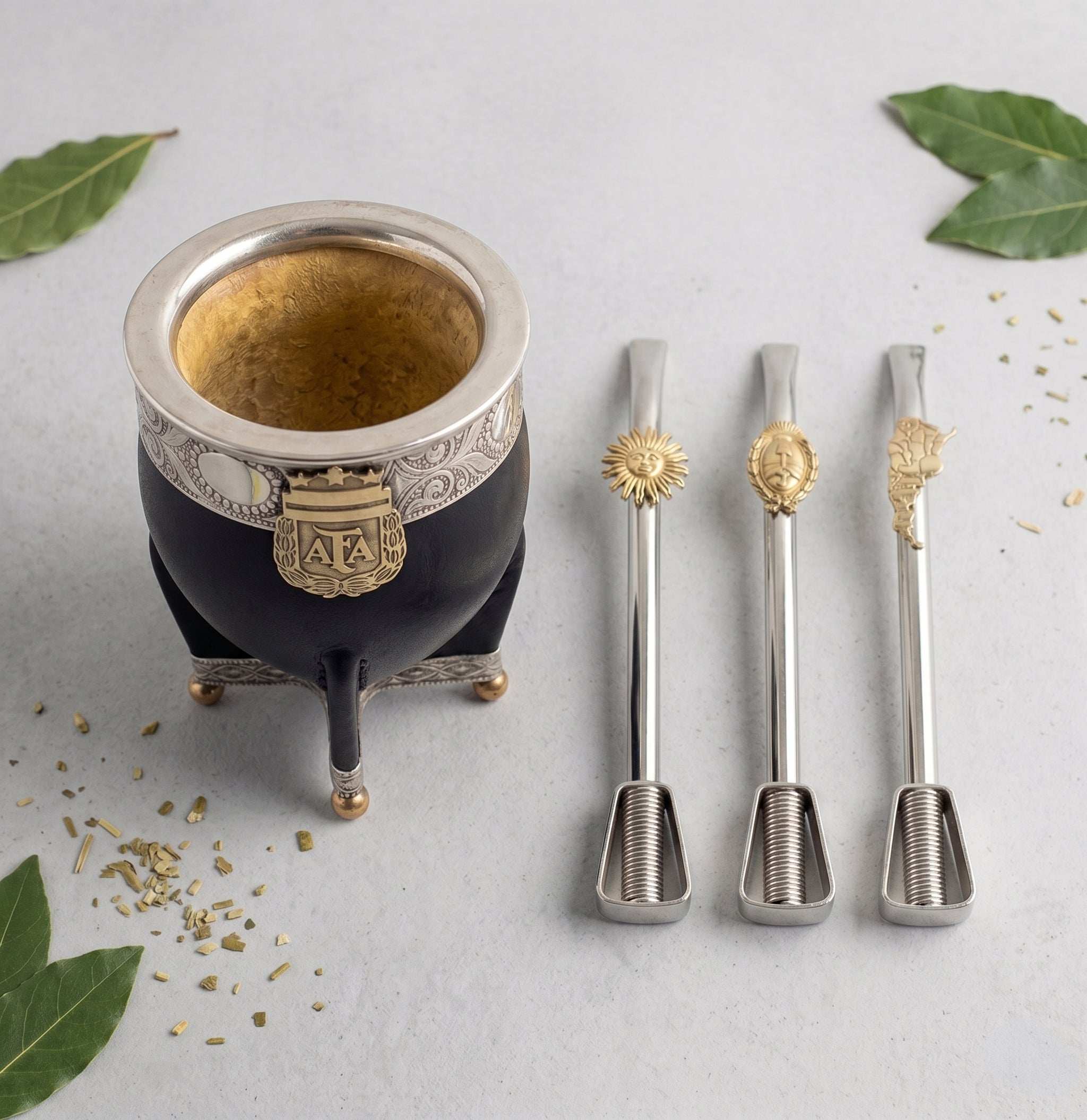 Three alpaca bombilla straw options with bronze accents—Sol de Mayo, Escudo shield, and Argentina map—displayed next to the Luv Mate Campeones AFA Imperial Mate Gourd featuring its 3-star alpaca rim and bronze shield emblem.
