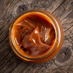 Top-down view of an open glass jar filled with rich, glossy San Ignacio Dulce de Leche on a rustic dark wood surface.