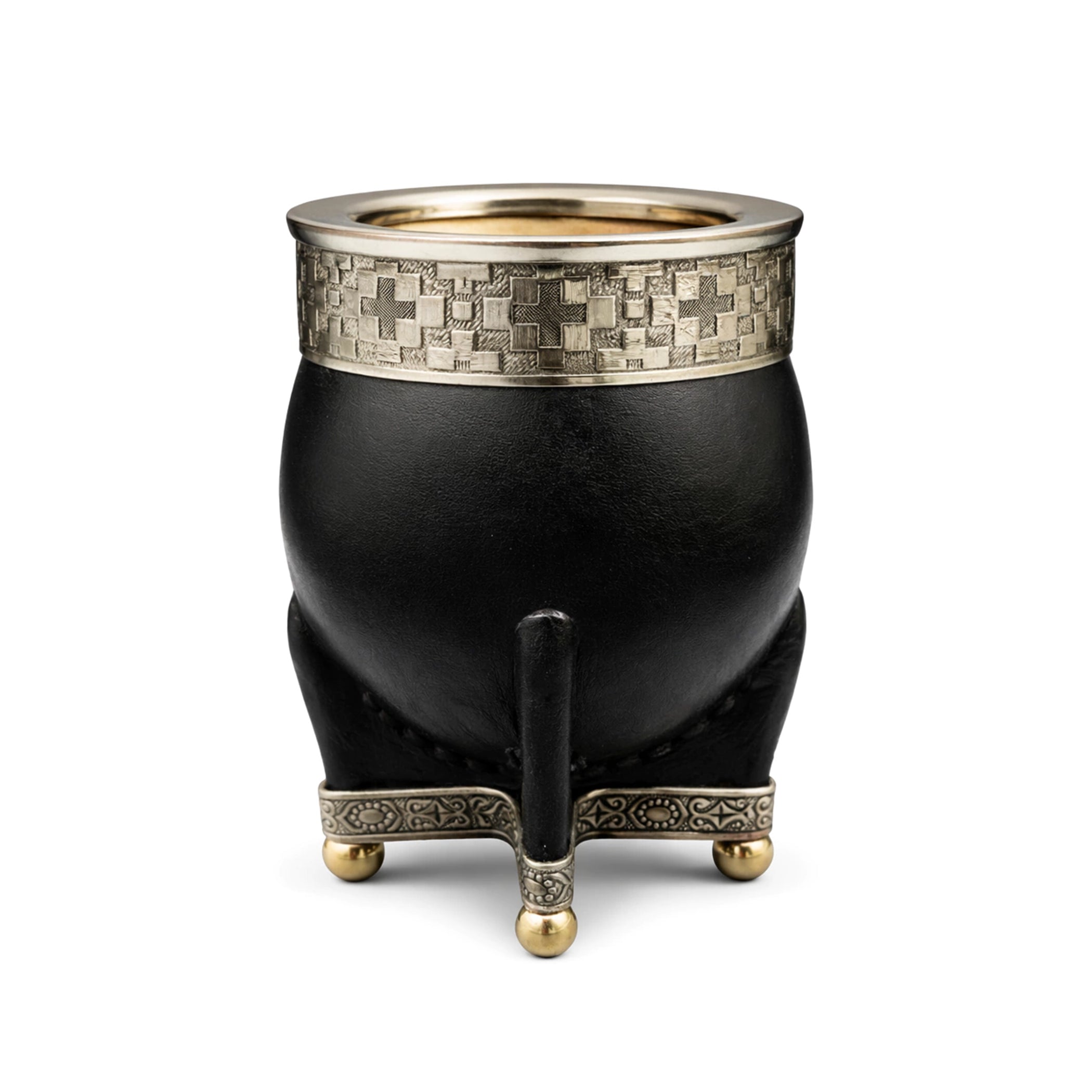Close-up shot of the Media Caña Chiseled Imperial Mate. The black leather gourd features a deeply patterned alpaca metal rim showing repeating cross motifs and a decorative footed base with bronze 'bolitas'. An interactive blue dot hotspot is prominent on the gourd body for feature exploration.