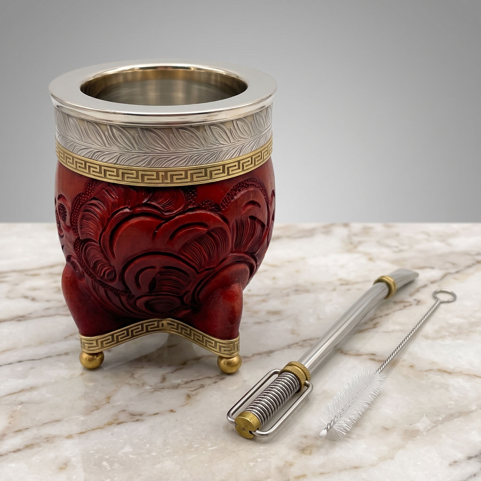 A carved malbec red Minue Federal mate and a stainless steel Limay bombilla with brass accents, presented on marble with a cleaning brush