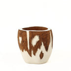A straight-on profile shot of a handcrafted mate gourd on a pure white background. The image highlights the organic brown and white piebald pattern on the exterior, inspired by the animal hides typical of the South American countryside.
