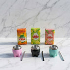 A product lineup of three colourful Milonga mate gourds (pink, black, and meadow green) paired with three packages of CBSé flavoured yerba mate (Naranja, Limón, and Pomelo), with silver and black bombilla straws on a white marble surface.