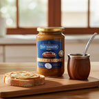 Jar of San Ignacio Dulce de Leche Traditional (450g) on a wooden board with a slice of toast and a mate gourd with bombilla.