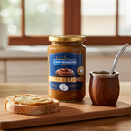 A glass jar of San Ignacio Dulce de Leche on a wooden board with a spread toast and a wooden mate gourd in a sunlit morning kitchen