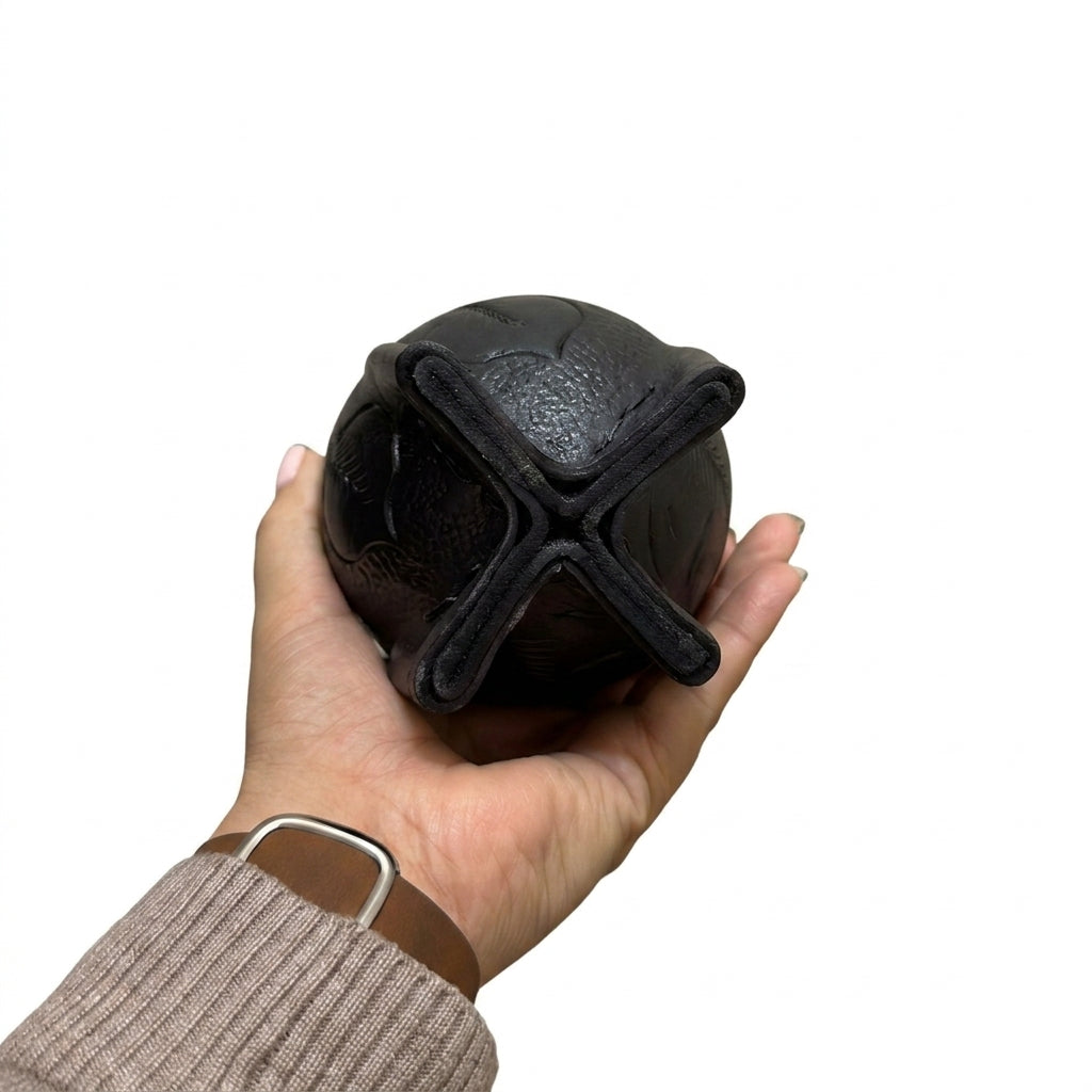Bottom view of a hand holding a black hand-embossed leather Imperial mate gourd, highlighting its reinforced four-legged base, set against a plain white background.