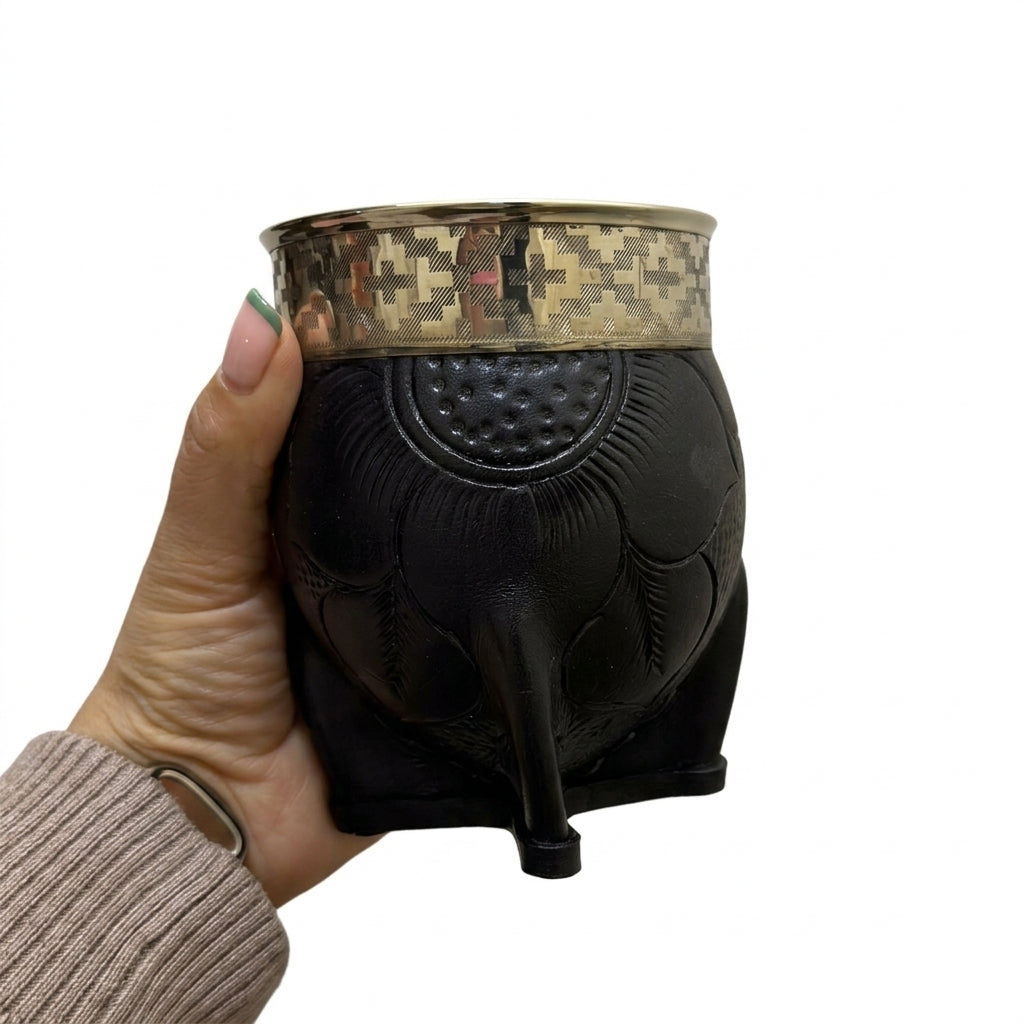 A hand holding a black hand-embossed leather Imperial mate gourd, showcasing its geometric Alpaca silver rim and floral leather detailing against a plain white background.