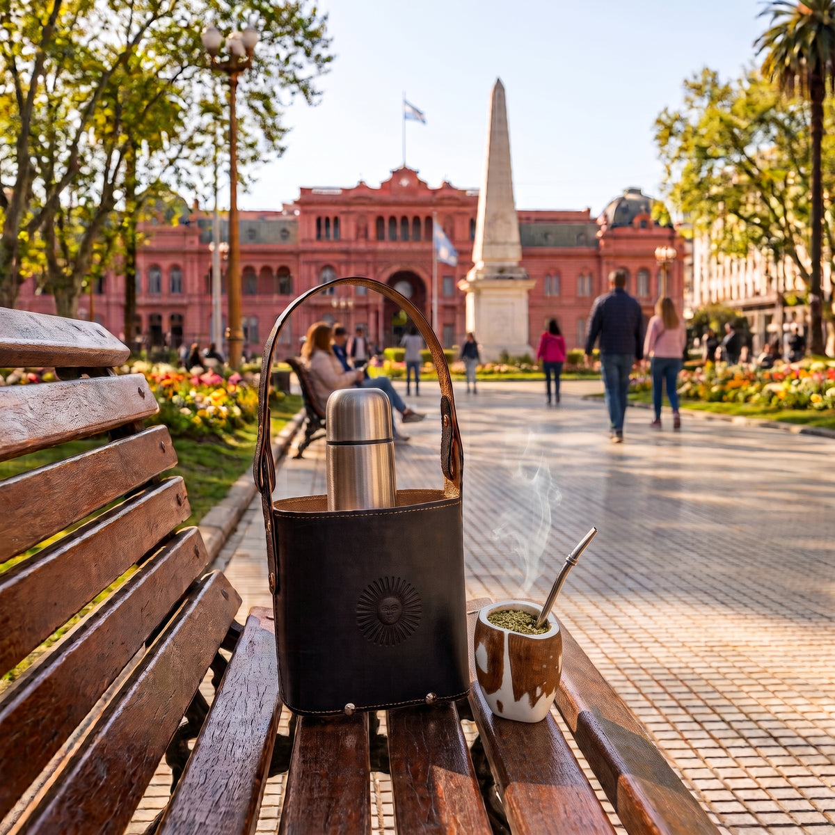 Outdoor lifestyle photo of a handcrafted black leather Criolla Matera with a thermos and a wooden mate, resting on a wooden bench in Plaza de Mayo.
