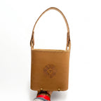 A hand holding a tan brown leather Criolla Matera from below, featuring a single top handle, an embossed Sun of May emblem on the front, and brass-tone rivets near the base, set against a plain white background.