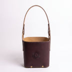 A dark brown leather Criolla Matera standing upright, featuring a top handle, brass rivets at the base, and an embossed Sun of May emblem on the front, set against a clean white background.