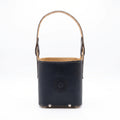 A black smooth leather Criolla Matera standing upright, featuring a top handle, fine contrast perimeter stitching, and an embossed Sun of May emblem on the front, set against a clean white background.