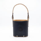 A black smooth leather Criolla Matera standing upright, featuring a top handle, fine contrast perimeter stitching, and an embossed Sun of May emblem on the front, set against a clean white background.