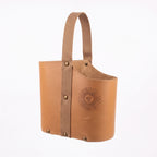 A light tan leather Uruguaya Matera featuring a matching beige woven strap, brass-tone rivets along the side and base, and an embossed Sun of May detail on the front, set against a plain white background.