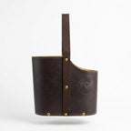 dark brown leather Uruguaya Matera featuring a matching brown woven nylon strap, brass-tone metal rivets along the base, and an embossed Sun of May design on the front, set against a plain white background.