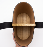 Top-down interior view of a black leather Uruguaya Matera, showing its textured tan leather lining, solid wooden base, central wooden divider, and black woven nylon straps against a white background.