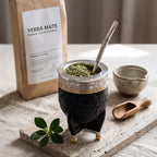 Luv Mate Minué Federal black hand-tooled leather Imperial mate cup with silver bombilla next to a kraft paper yerba mate bag.