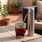 Premium Malbec red Imperial mate gourd with chiseled alpaca silver rim and bronze feet, paired with a sleek stainless steel thermos in a sunny outdoor setting.