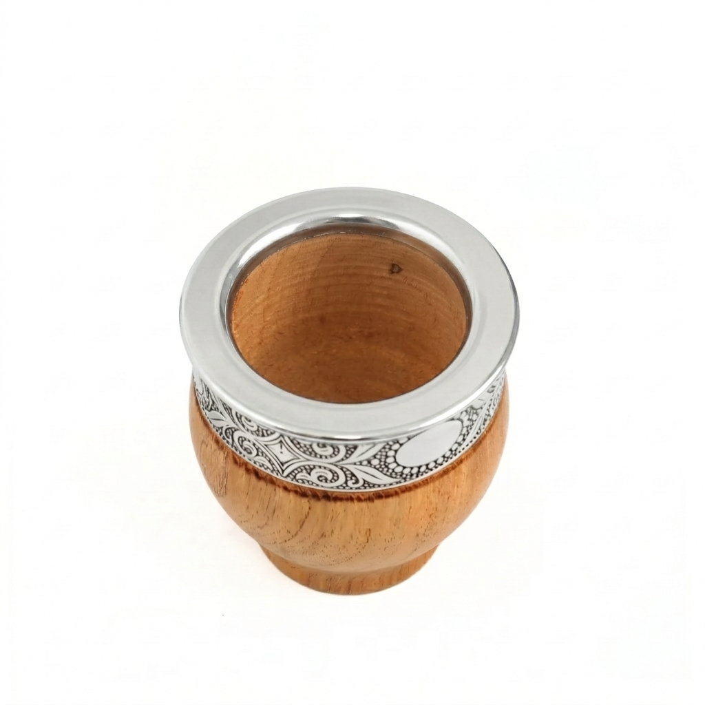 A handcrafted wood mate gourd with an intricately hand-chiseled polished metal virola (rim) featuring two prominent smooth reflective medallions on the front, viewed from an elevated perspective against a white background.